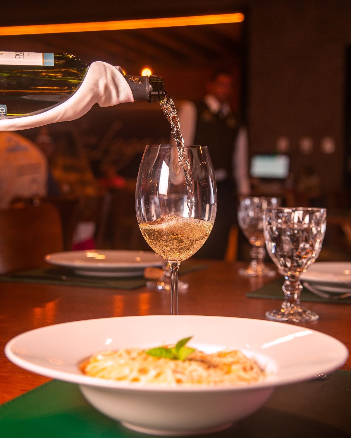 Vinho sendo servido à mesa, ao lado de um prato de massa